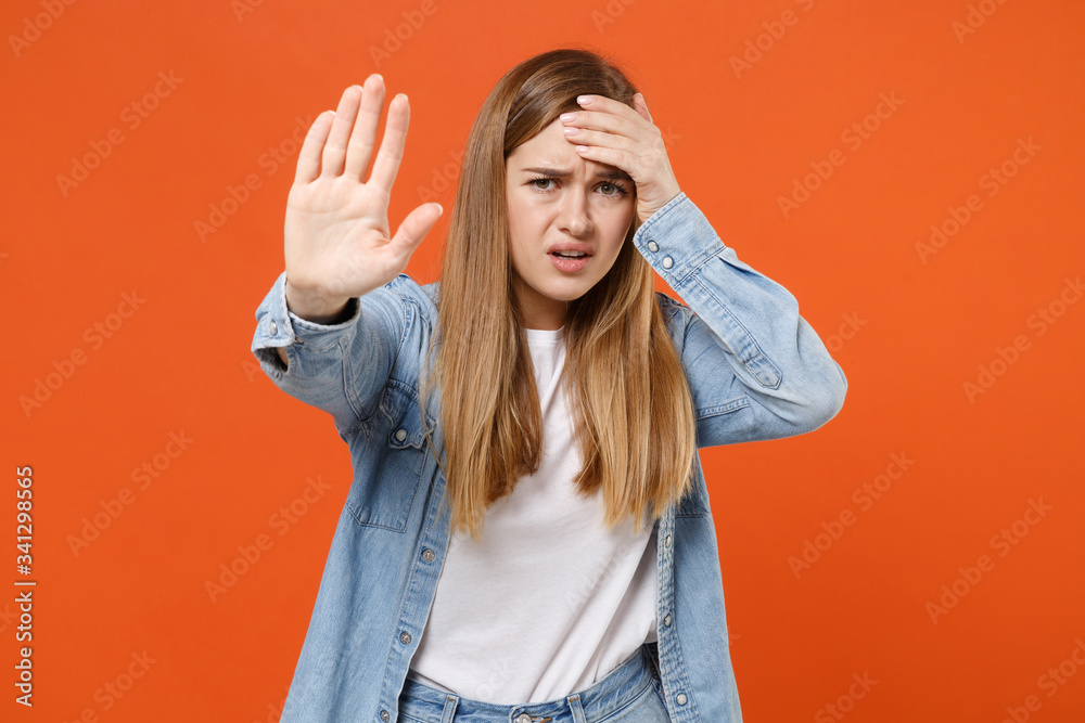 Worried young woman girl in casual denim clothes posing isolated on orange background studio portrait. People lifestyle concept. Mock up copy space. Showing stop gesture with palm, put hand on head. Worried young woman girl in casual denim clothes posing isolated on orange background studio portrait. People lifestyle concept. Mock up copy space. Showing stop gesture with palm, put hand on head.