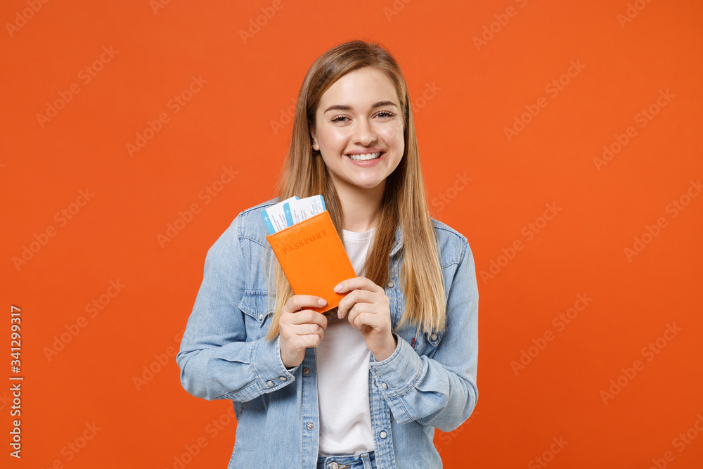 Smiling young woman girl in casual denim clothes posing isolated on orange wall background studio portrait. People emotions lifestyle concept. Mock up copy space. Hold passport ticket boarding pass. Smiling young woman girl in casual denim clothes posing isolated on orange wall background studio portrait. People emotions lifestyle concept. Mock up copy space. Hold passport ticket boarding pass.