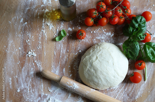 Il concetto di cibo italiano. Pasta per pizza e ingredienti freschi: pomodori ciliegia, foglie di basilico, aglio, olio d'oliva sulla tavola di legno rustica. Disteso, spazio per il testo.