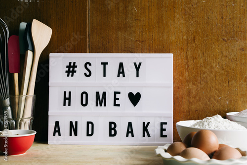 Stay home and bake covid 19 conceptual image for coronavirus pandemia,  with a lightbox texting stay home and bake,circled by tools and ingredients for baking bread and cake during qarantine photo