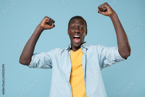 Crazy young african american man guy in casual shirt, yellow t-shirt posing isolated on blue background. People lifestyle concept. Mock up copy space. Screaming, expressive gesticulating with hands.