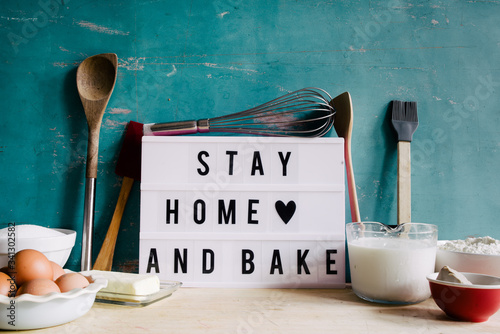Stay home and bake covid 19 conceptual image for coronavirus pandemia,  with a lightbox texting stay home and bake,circled by tools and ingredients for baking bread and cake during qarantine photo