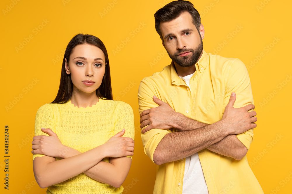 Young couple with crossed arms looking at camera on yellow background Young couple with crossed arms looking at camera on yellow background