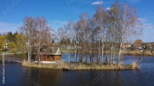 Morning landscape, wooden hunting lodge, on a small man-made island. A wooden platform is coming to the house, birch trees are growing on both sides. Village of Old Solotvin photo