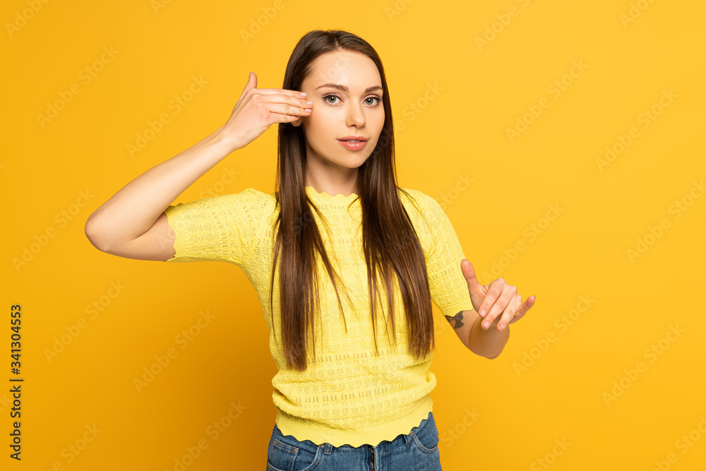 Young woman gesturing while using deaf and dumb language on yellow background Young woman gesturing while using deaf and dumb language on yellow background
