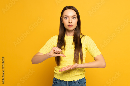 Beautiful woman gesturing while using sign language on yellow background