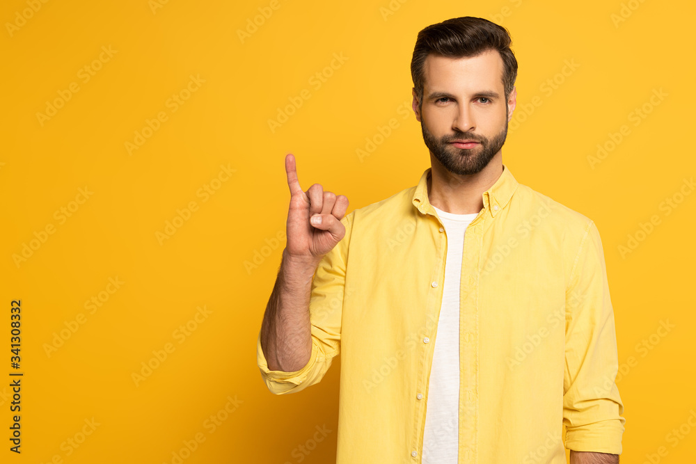 Handsome man showing letter in deaf and dumb language on yellow background Handsome man showing letter in deaf and dumb language on yellow background
