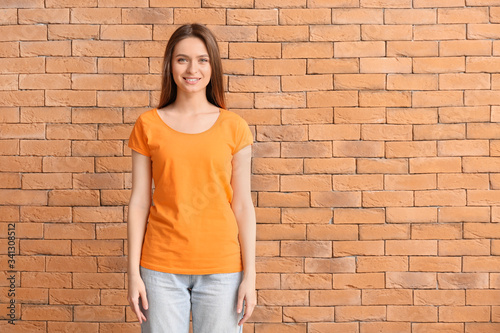 Young woman in stylish t-shirt on brick background © Pixel-Shot