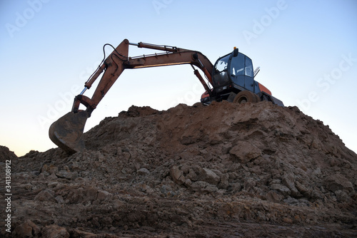 Bucked wheel excavator on earthmoving. Backhoe digs ground in sand quarry on blue sky background. Construction machinery for excavation, loading, lifting and hauling of cargo on job sites