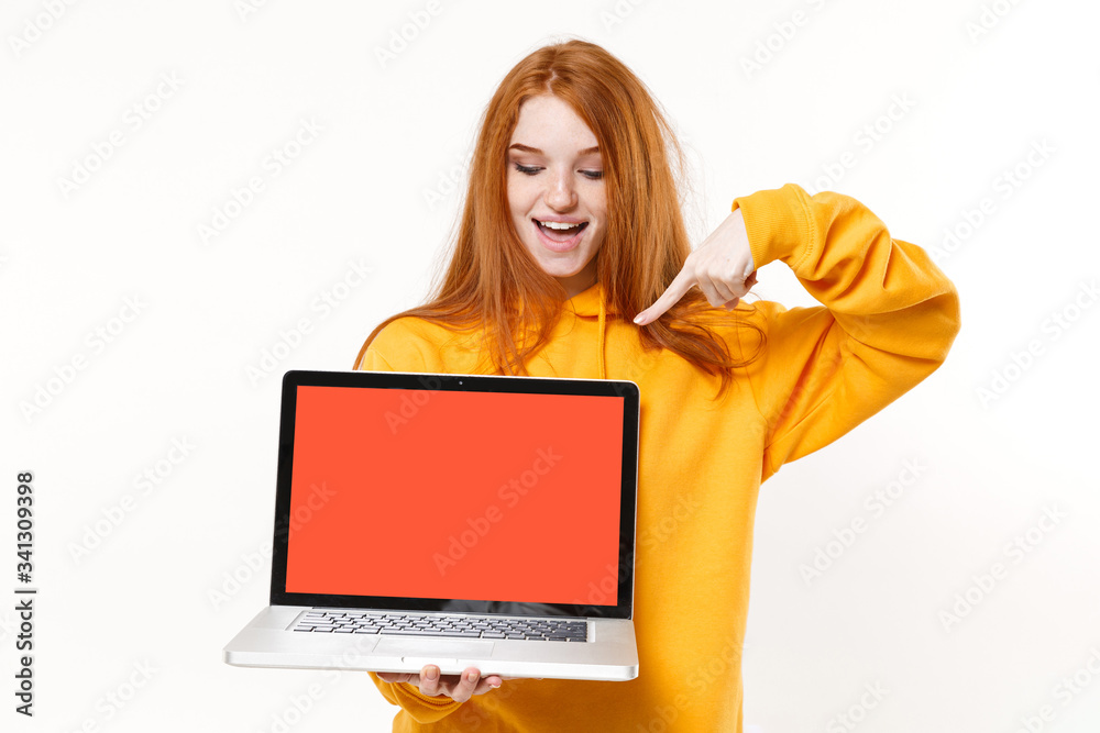 Naklejka premium Funny young redhead woman girl in yellow hoodie posing isolated on white background. People lifestyle concept. Mock up copy space. Pointing index finger on laptop pc computer with blank empty screen.