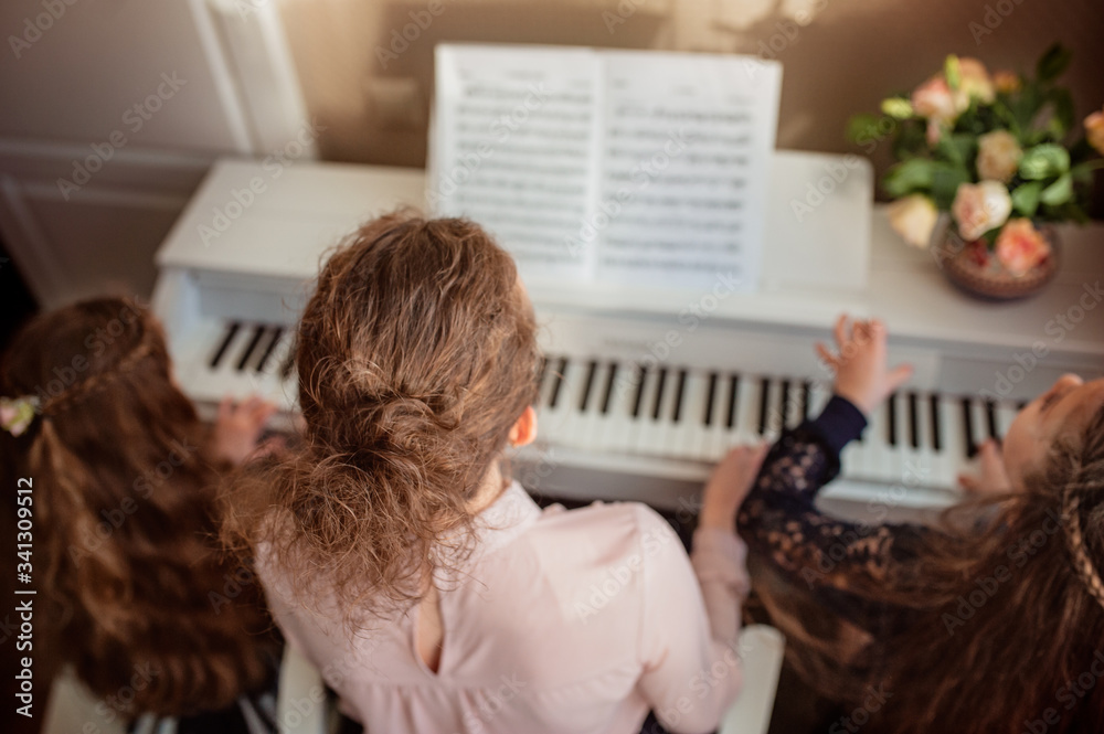 Home piano lesson. A woman and two girls practice sheet music on one musical instrument. Family