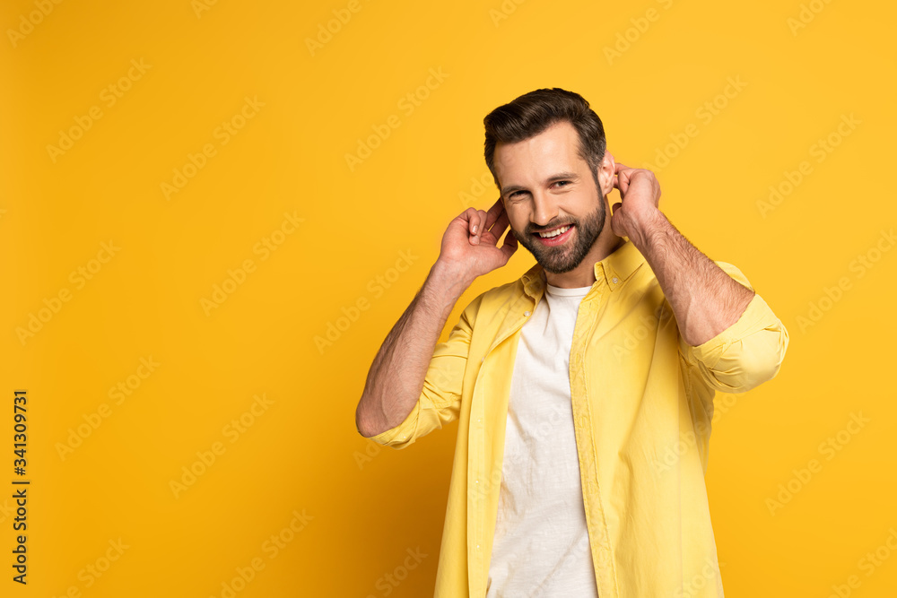 Smiling man showing gesture in deaf and dumb language on yellow background Smiling man showing gesture in deaf and dumb language on yellow background