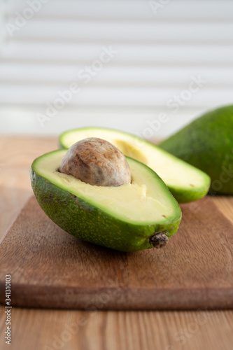 Close-up of half an avocado and another whole one, with selective focus, on wooden board and white background, in vertical, with copy space