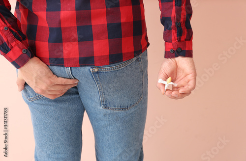 Young man with hemorrhoidal suppository on color background
