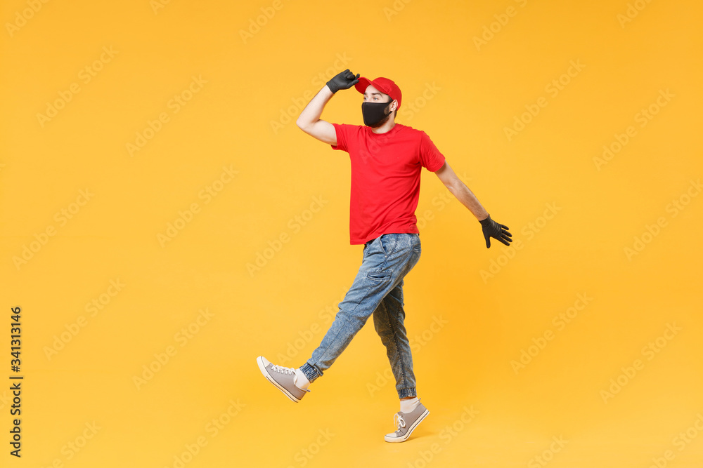 Full length delivery man in red cap t-shirt uniform sterile face mask gloves isolated on yellow background studio Guy employee courier Service quarantine pandemic coronavirus virus 2019-ncov concept. Full length delivery man in red cap t-shirt uniform sterile face mask gloves isolated on yellow background studio Guy employee courier Service quarantine pandemic coronavirus virus 2019-ncov concept.