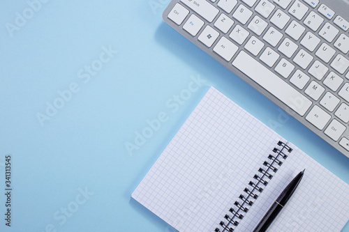 Minimal work space. Creative flat lay photo of workspace desk. Top view office desk with notepad, keyboard, paper notepad and supplies on blue color background. Work from home idea.