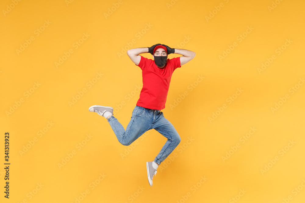 Fun jumping delivery man in red cap t-shirt uniform sterile face mask gloves isolated on yellow background studio Guy employee courier Service quarantine pandemic coronavirus virus 2019-ncov concept.