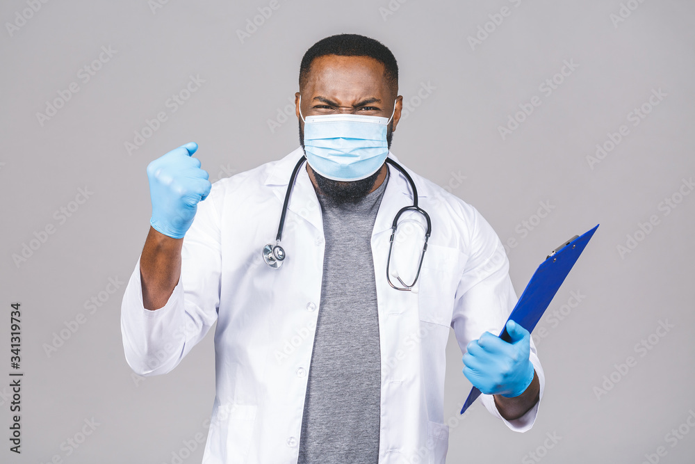 African american doctor man in medical gown face mask gloves isolated on grey background. Epidemic pandemic coronavirus 2019-ncov sars covid-19 flu virus. Holding clipboard. African american doctor man in medical gown face mask gloves isolated on grey background. Epidemic pandemic coronavirus 2019-ncov sars covid-19 flu virus. Holding clipboard.