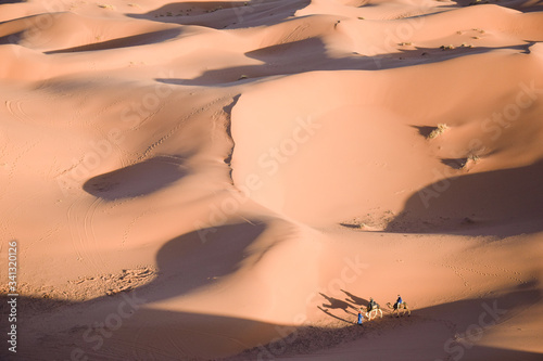 Desierto del Sahara con grandes dunas y un grupo de personas y camellos a distancia