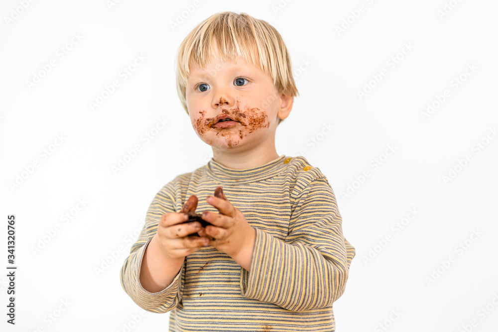 Cute blond dirty toddler eating chocolate bar with great pleasure Cute blond dirty toddler eating chocolate bar with great pleasure