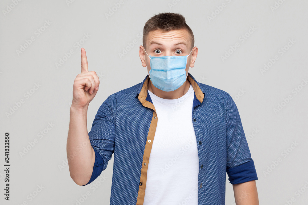 Idea. Portrait of excited young man in casual style with surgical medical mask standing, finger up and looking at camera with surprised face. indoor studio shot, isolated on gray background.