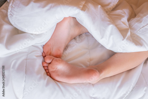 Child feet under the white blanket. Tenderness of morning dream