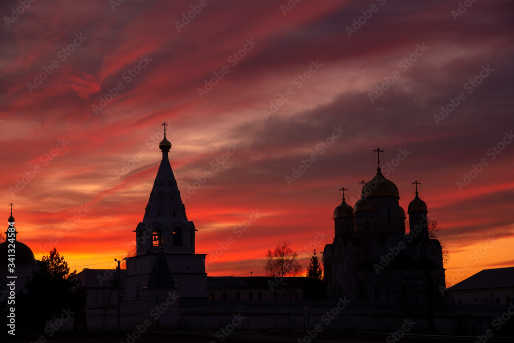 The black silhouette of the monastery against the bright sunset sky.