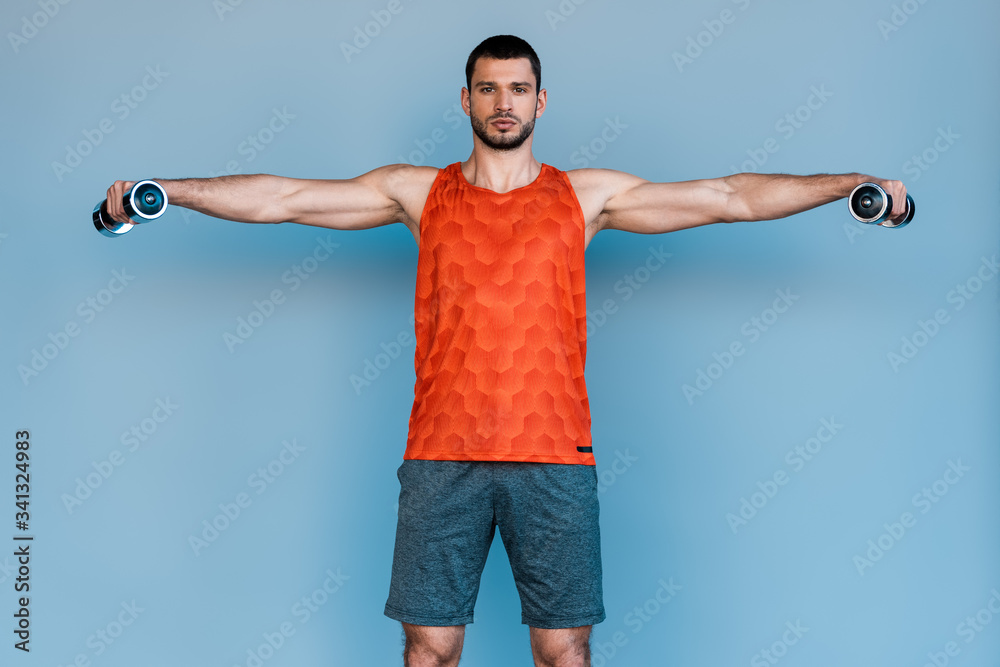 Naklejka premium bearded sportsman standing with outstretched hands and exercising with dumbbells on blue