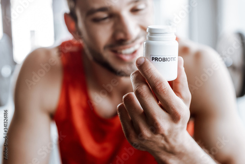 Foto selective focus of happy sportsman holding bottle with probiotic lettering in gy