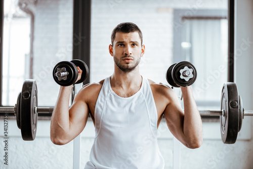 athletic sportsman holding dumbbells while working out in gym