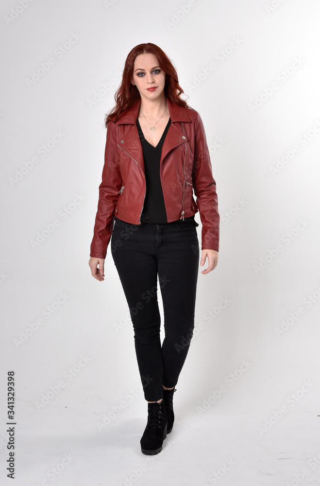 Portrait of a pretty girl with red hair wearing black jeans and boots with leather jacket. full length standing pose on a studio background. Portrait of a pretty girl with red hair wearing black jeans and boots with leather jacket. full length standing pose on a studio background.