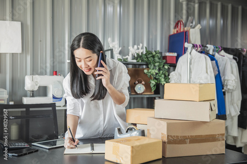 Young business woman working online e-commerce shopping at her shop. Young woman seller prepare parcel box of product for deliver to customer. Online selling, e-commerce.