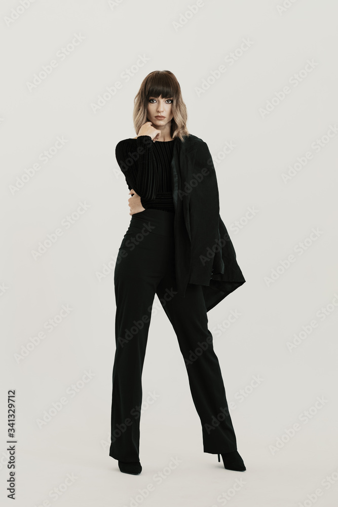 Full length portrait, beautiful woman with attitude wearing black clothes posing on white background looking at the camera Full length portrait, beautiful woman with attitude wearing black clothes posing on white background looking at the camera