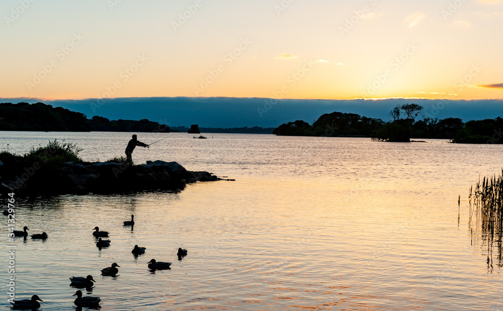 Naklejka premium Silhouette of man casting a fishing rod on the lakes of Killarney national park at sunset