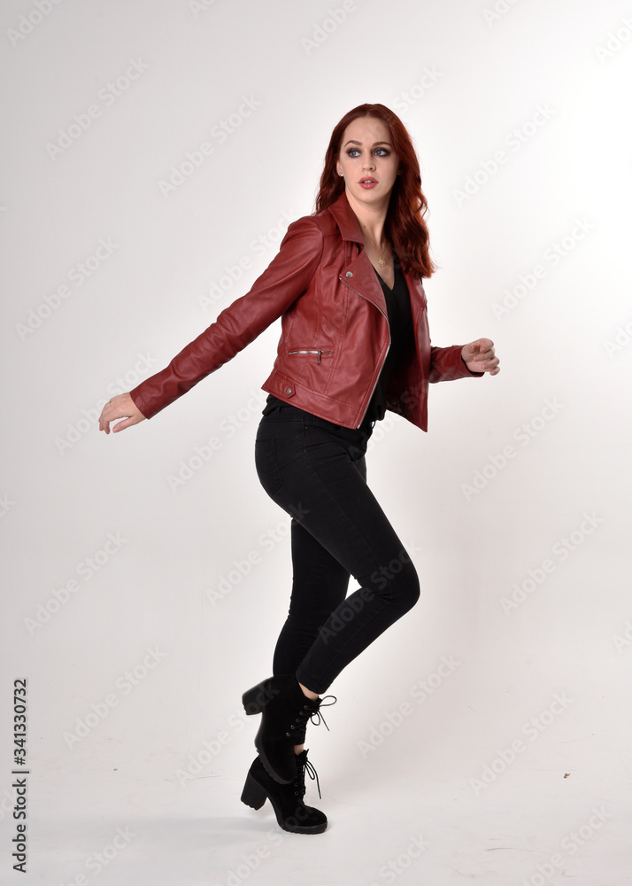 Portrait of a pretty girl with red hair wearing black jeans and boots with leather jacket. full length standing pose on a studio background. Portrait of a pretty girl with red hair wearing black jeans and boots with leather jacket. full length standing pose on a studio background.
