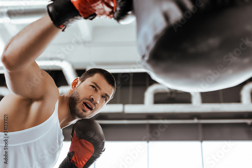selective focus of bearded sportsman in boxing gloves exercising with punching bag
