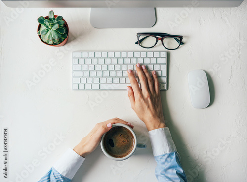 Top view of a white office desk table with female elegant hands, a laptop keyboard, smartphone, a cup of coffee and a green flower succulent. Copy space, flat lay. .Business concept, technology.