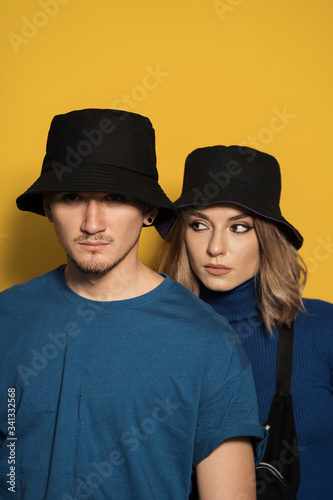 Portrait young pretty man and woman in blue t-shirts and black caps posing on yellow background © arthurhidden