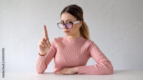 Fototapeta Naklejka Na Ścianę i Meble -  Portrait Of Young Woman Wearing Hipster Glasses On home. girl raises index finger
