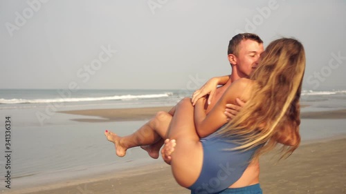 A man carries a woman in his arms along the beach. Young couple in love is resting on the sea