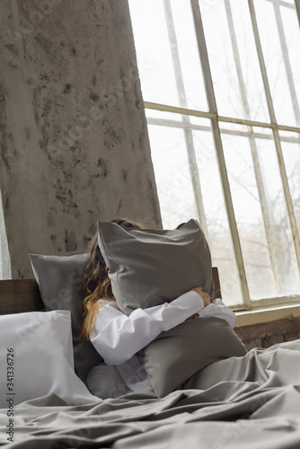 woman hugging pillow, pillow made of silk fabric, quality bedding, large window in the interior