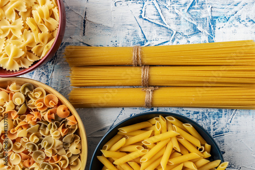 bundles of spaghetti and ceramic bowls with various pastas on a blue and white textured background