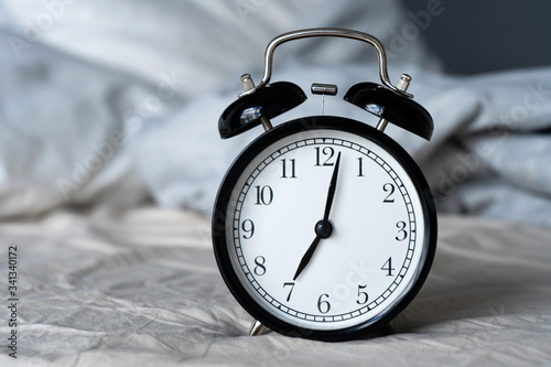 Stylish alarm clock with a bell. The hands show 7 hours. Wake up time