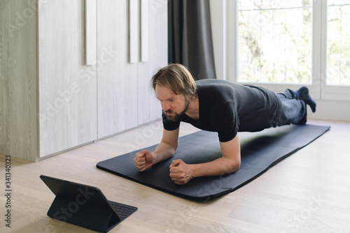 Mann macht Planks zu Hause mittels online Kurs photo