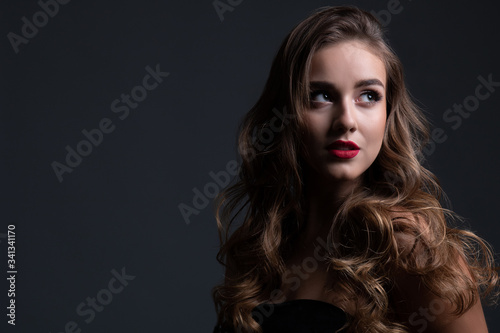 Close up beauty portrait of young beautiful girl in shadow with long curly hair and perfect make up wearing a black dress. Text space.