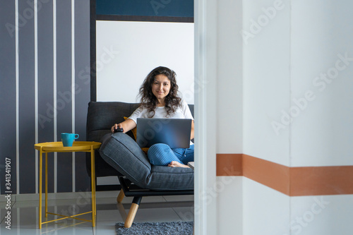 Beautiful girl sitting with a laptop on a sofa in a stylish room. Work from home. Work atmosphere in a good mood © Kate
