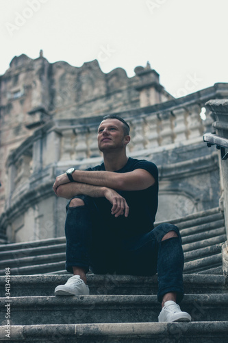 guy sits on the stairs in the street in the background architectural house.