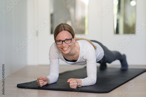 Junge Frau macht Planks zu Hause auf der Fitnessmatte und lächelt in die Kamera photo