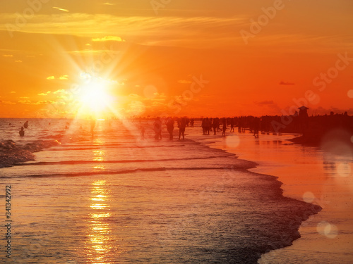 group of silhouetted people on public beach over orange colored sunset sky in Siesta key, Sarasota, Florida
