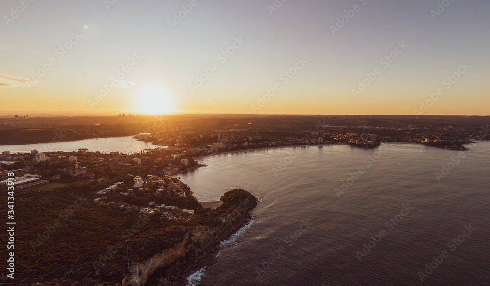 Panoramic aerial drone sunset view of Manly Beach, an affluent seaside suburb of Sydney, New South Wales, Australia. Manly Wharf on the left side.